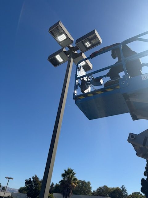 Electrician on a lift beside a four-head parking lot light
